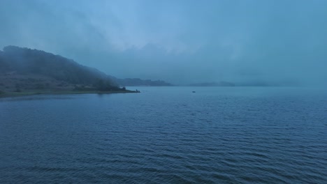 Nebliger-Morgen-Am-Nanclares-De-Gamboa-See,-Baskenland,-Mit-Ruhigem-Wasser-Und-Sanften-Sonnenstrahlen
