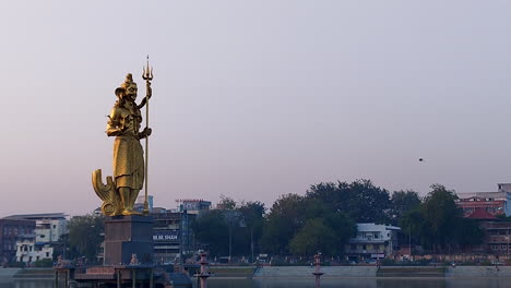 Enjoy-a-beautiful-side-view-of-the-immense-gilded-Lord-Shiva-statue-in-Sursagar-Lake,-Vadodara,-as-dusk-settles,-creating-a-serene-and-enchanting-atmosphere