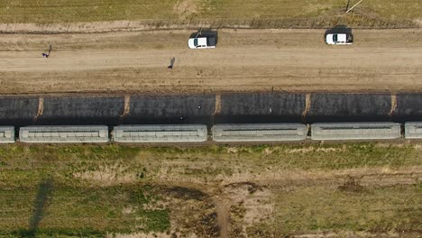 Aerial-shot-of-a-train-moving-along-tracks-in-rural-Argentina,-flanked-by-roads-and-vehicles
