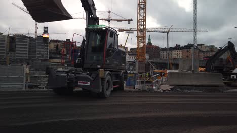Tractor-and-yellow-dressed-worker-move-through-frame-at-construction-site-in-Stockholm