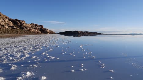 Schwenk-Zur-Glasig-Reflektierenden-Oberfläche-Des-Salzsees-Von-Uyuni,-Bolivianische-Hochebene