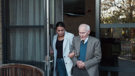 Elderly-man-being-escorted-through-door-by-caregiver-for-healthy-walk-outside