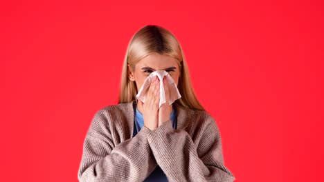 Sick-blonde-woman-sneezes-in-handkerchief,-concept-allergic-to-hay,-red-background