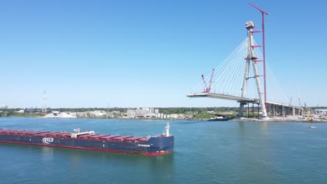 Cargo-vessel-sail-under-Gordie-Howe-international-bridge-being-built-over-Detroit-River,-aerial-view