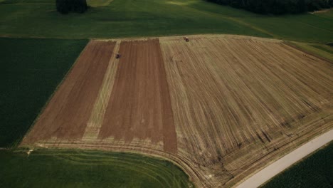 Tractors-working-on-the-vast-golden-fields-at-dusk,-aerial-view