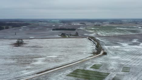 Aerial-view-of-frozen-farmland-and-countryside-gravel-road-tree-line-in-winter