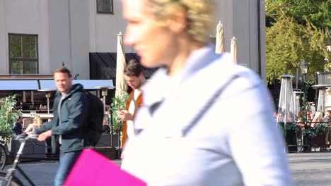 People-sit-at-outdoor-restaurant-in-sunlight-in-Stockholm-as-others-pass-in-foreground