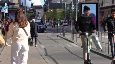 People-walking,-riding-bikes-and-kick-scooters-on-Stockholm-street