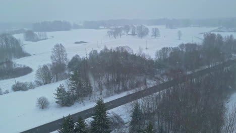 Aerial-view-flying-over-a-countryside-road,-during-blizzard-on-a-gloomy-winter-day