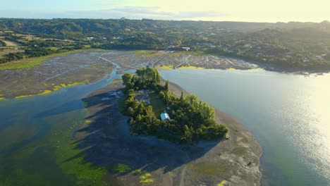Drone-circling-the-Aucar-Island,-overlooking-a-cemetery-and-a-chapel,-in-sunny-Chiloe