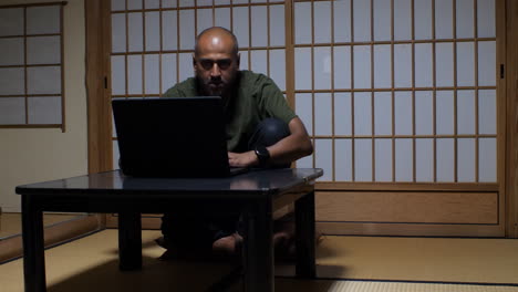 In-a-traditional-Japanese-ryokan,-a-bald-man-seamlessly-integrates-modern-technology-into-the-serene-ambiance