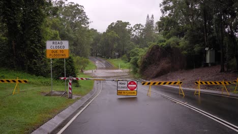 Gold-Coast,-Queensland,-16-February-2024---Wide-shot-of-road-closure-signage-and-flooding-across-Hardy's-Road-in-Mudgeeraba-after-heavy-rains-continue-to-lash-South-East-Queensland,-Australia