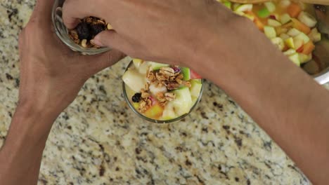 Overhead-view-of-a-man-adding-granola-to-fruit-cocktail