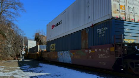 Eine-Aufnahme-Aus-Niedriger-Perspektive-Eines-Langen-Güterzuges-Mit-Voller-Ladung,-Bedeckt-Mit-Graffiti-An-Einem-Sonnigen-Tag-Mit-Klarem-Blauen-Himmel