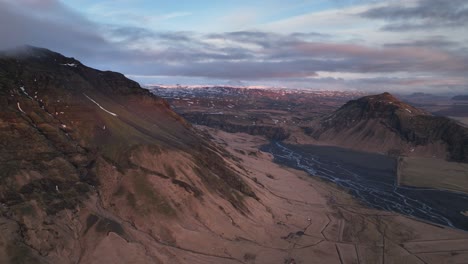 Aerial-landscape-view-of-a-river-flowing-down-from-a-mountain-valley,-in-Iceland,-on-a-cloudy-evening