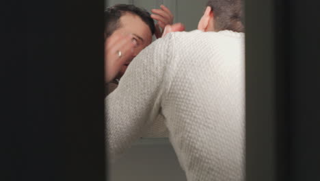 Man-examining-receding-hairline-in-a-bathroom-mirror,-concern-visible,-in-natural-light