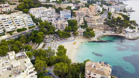 Playa-Illetas-Con-Aguas-Cristalinas,-Bañistas-Y-Edificios-Circundantes-En-Un-Día-Soleado,-Toma-De-Drones,-Vista-Aérea