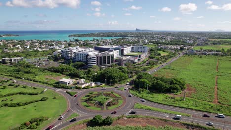Aerial-shot-of-La-Croisette-in-Mauritius,-showcasing-a-bustling-roundabout,-green-landscapes,-and-distant-ocean-views,-bright-day