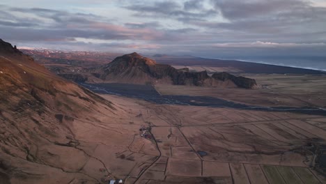 Aerial-panoramic-view-of-a-river-flowing-down-from-a-mountain-valley,-in-Iceland,-on-a-cloudy-evening
