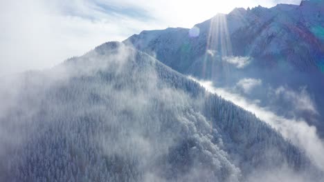 Snowy-Bucegi-Mountains-peaking-through-clouds,-aerial-view