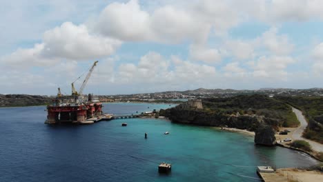Tugboat-beach-in-curacao,-bright-day-with-clear-waters-and-rugged-coastline,-industrial-harbor,-aerial-view