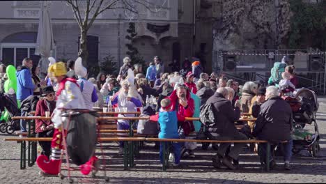People-in-costumes-sit-on-benches-at-tables-in-a-festival-area-during-the-Gnoccolada-carnival-in-the-city-center-of-Brixen---Bressanone,-South-Tyrol-Italy
