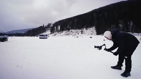 Person-stand-near-snowy-race-track-and-film-winter-drift-event-near-forest