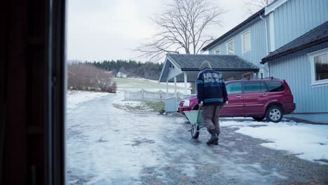 A-Man-is-Pushing-a-Wheelbarrow-Along-an-Icy-Road-to-Transport-Materials-Required-for-the-DIY-Hot-Tub---Static-Shot