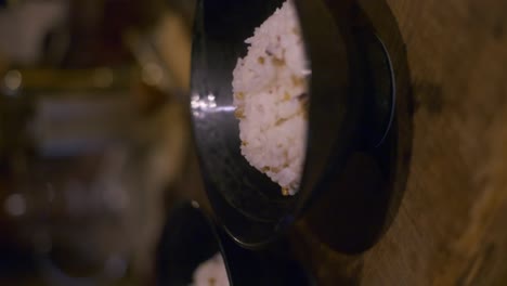 2-black-bowls-filled-with-rice-sitting-to-cool-on-wooden-tabletop,-filmed-as-vertical-slow-motion-closeup-slider-style-shot