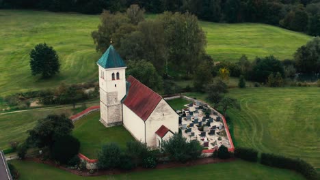 A-quaint-countryside-church-surrounded-by-lush-greenery,-overcast-sky,-aerial-view
