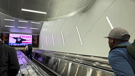 Pasajeros-Que-Viajan-En-Escaleras-Mecánicas-Para-Reclamar-Bolsas-En-La-Terminal-Nacional-Del-Aeropuerto-Internacional-Hartsfield-Jackson-De-Atlanta,-Vistos-Desde-Las-Escaleras-Mecánicas-En-Una-Terminal-Recientemente-Remodelada-Y-Bien-Iluminada