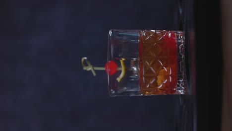 Altmodischer-Cocktail,-Chilenische-Version-Mit-Bourbon-Whiskey,-Zucker,-Eis,-Bitteren-Tropfen,-Maraschinokirsche-Auf-Dunklem-Hintergrund-Und-Selektivem-Fokus,-Vertikales-Video