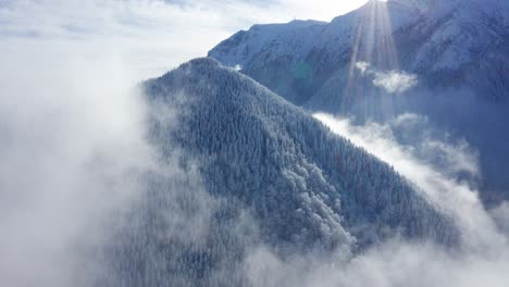 Snow-covered-Bucegi-Mountains-peaking-through-clouds,-with-sunlight-rays