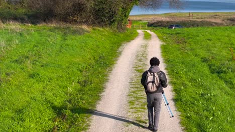 Back-View-Of-Man-Carrying-Tripod-While-Walking-On-Rural-Trail