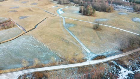 Aerial-view-of-frozen-farmland-meadow-and-countryside-gravel-road