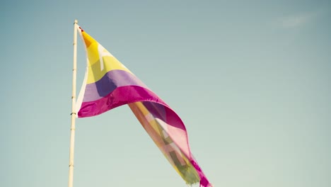 Colorful-peace-flag-fluttering-in-the-breeze-against-a-clear-blue-sky,-vibrant-symbol-of-harmony