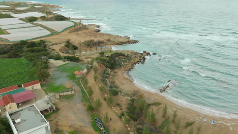 Die-Luftaufnahme-Von-Kapparis-In-Paralimni,-Zypern,-Zeigt-Eine-Ruhige-Küstenregion,-In-Der-Landwirtschaftliche-Felder-Auf-Sandstrand-Und-Felsige-Küstenlinie-Treffen-Und-Sich-Das-Mittelmeer-Bis-Zum-Horizont-Erstreckt