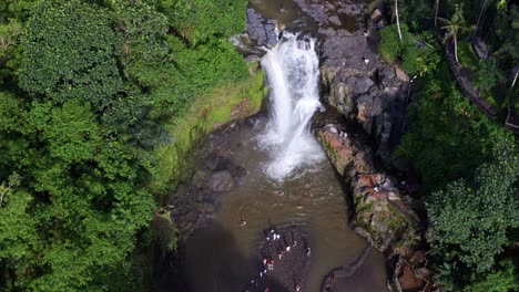 Top-down-view-of-Tegenungan-Waterfall-natural-Pool-with-Tourists-swimming-and-standing---BALI,-Indonesia
