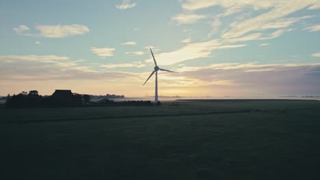 Turbina-Eólica-Girando-En-Silueta-Contra-Un-Vibrante-Amanecer,-Entorno-Rural-Con-Horizonte-Despejado