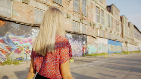 Young-blond-woman-walking-through-factory-area-covered-with-artistic-murals
