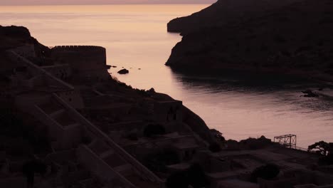 Drone-descends-across-old-abandoned-prison-ruins-of-Spinalogka-Island-Greece,-establish-at-sunset