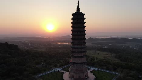 Drone-aerial-view-in-Vietnam-flying-around-a-buddhist-pagoda-in-a-Ninh-Binh-temple-at-sunset-with-green-landscape-in-the-horizon