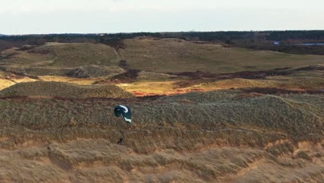 Medium-dynamic-aerial-shot-of-a-paraglider-sailing-over-sand-dunes-with-the-Noordhollands-Duinreservaat-in-the-background