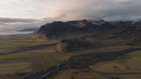 Aerial-panoramic-landscape-view-of-a-river-flowing-down-from-a-mountain-valley,-in-Iceland,-with-a-dramatic-evening-cloudscape