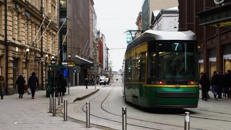 Green-tram-moving-through-Helsinki-streets-with-pedestrians,-daytime,-urban-scene,-city-life