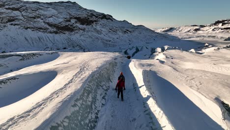 Aerial-landscape-view-over-two-people-hiking-on-a-expedition-on-Sólheimajökull-glacier,-in-Iceland