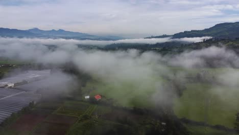 Slow-moving-drone-clip-over-a-green-field-and-the-clouds-with-the-volcano-Volcan-Pasochoa-and-the-Volcano-Padre-Encantado-at-the-background