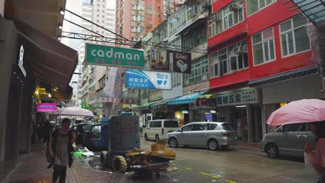 Straße-In-Hongkong-Mit-Fußgängerinnen,-Die-An-Einem-Bewölkten-Tag-Mit-Sonnenschirmen-Entlanglaufen