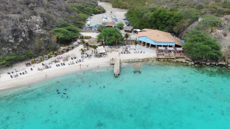 Kokomo-beach-in-curacao-with-people-swimming-and-lounging-on-the-sand,-vibrant-turquoise-water,-aerial-view