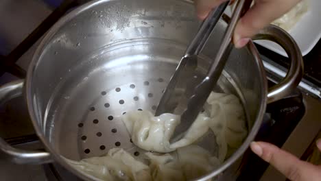 A-cooking-chef-uses-a-metal-grabber-to-retrieve-dumplings-from-a-metal-bowl,-epitomizing-the-art-of-culinary-preparation-and-food-crafting